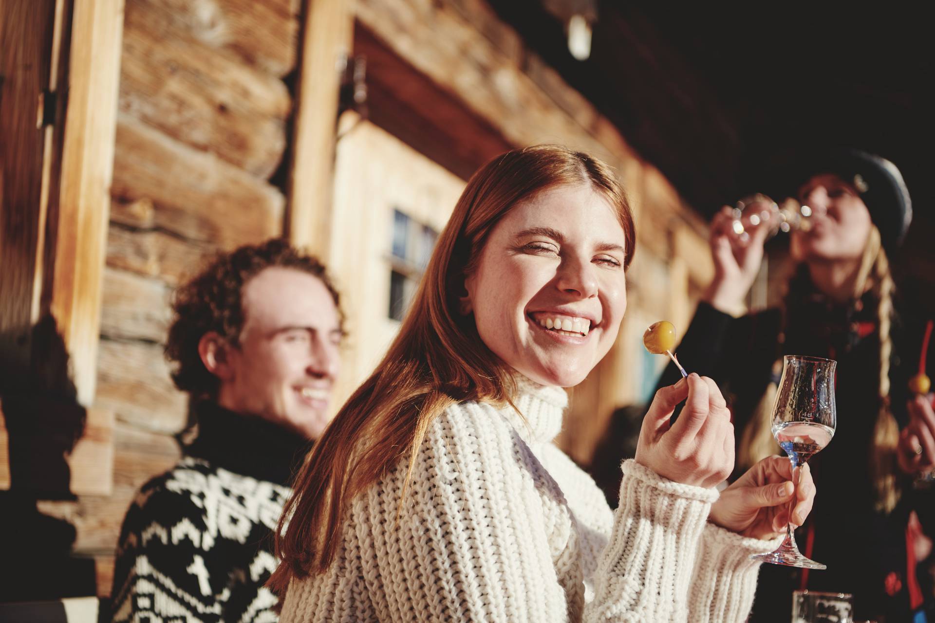 Frau hält eingelegte Mirabelle und Schnaps in der Hand vor einer rustikalen Berghütte