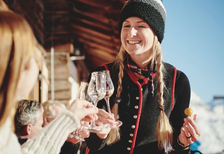 Frau hält eingelegte Mirabelle und Schnaps in der Hand vor einer rustikalen Berghütte