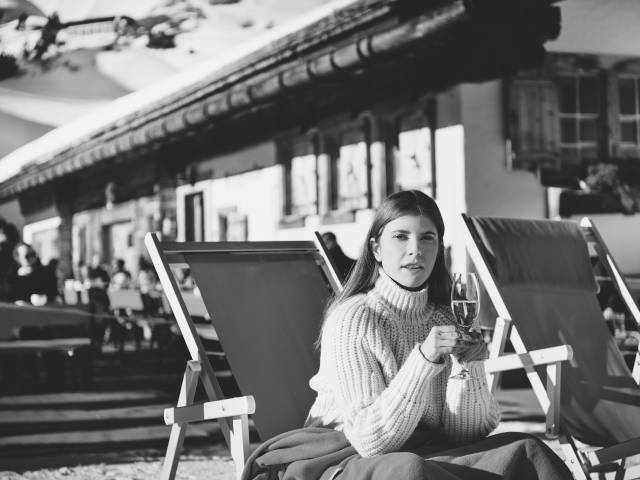 Frau sitzt in Sonnenstuhl und trinkt ein Glas Sekt